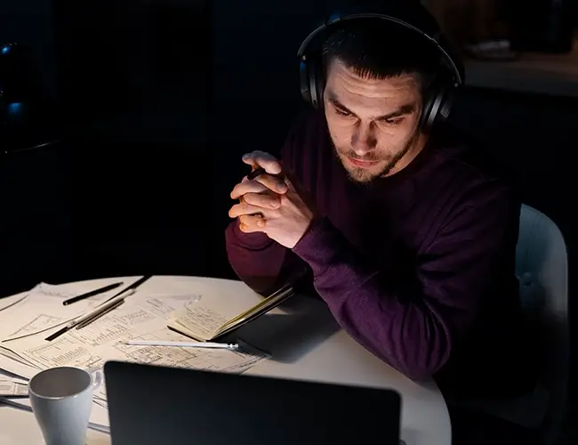 Man looking at laptop in the dark with headphones on